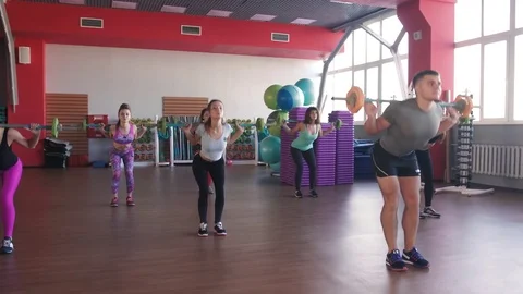 Quats with weights on training. Group of young women and man in aerobics class Видео 75869701