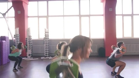 Quats with weights on training. Group of young women and man in aerobics class Видео 75869751
