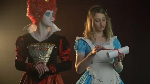 Queen of Hearts stands next to Alice while she reads the scroll Stock Footage 76455078