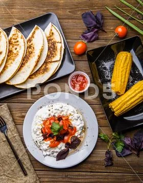 Quesadilla, salad with cottage cheese and tomatoes, two corn on wood table. Stock Photos