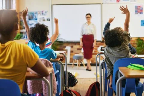 Question, hands up and children in classroom with teacher for lesson, learning Stock Photos