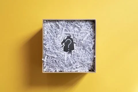 Question mark and shredded paper in abox against yellow background. Stock Photos