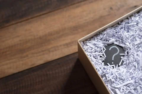 Question mark in a box with shredded paper on wooden table. Stock Photos