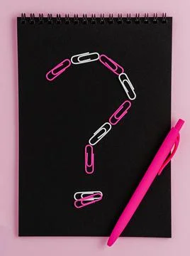 Question mark made of clips on black notebook blank on pink background. Fla.. Stock Photos