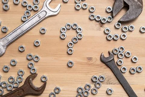 Question mark made of metal nuts on a wooden table, a variety of wrenches l.. 스톡 사진