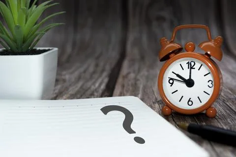 Question mark on notepad alarm clock set at 10 oclock on wooden background. Stock Photos