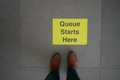 Queue starts here sign on the floor with boots below 스톡 사진