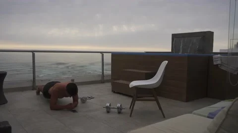 Quick camera of a man doing plank exercises on a terrace of a beach house next 스톡 동영상 192955154
