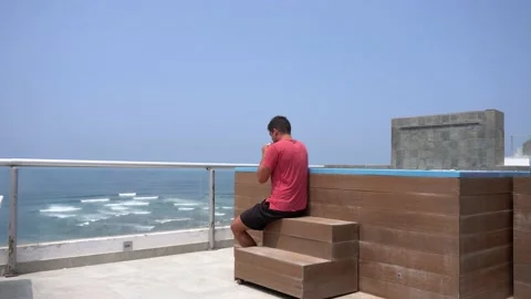 Quick camera of a man sitting drinking coffee at the edge of a pool on a terrace Stock Footage 194473643