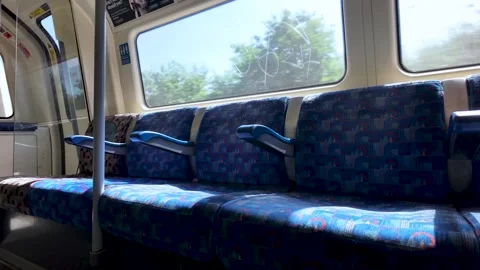 A quiet, empty row of blue patterned seats inside a modern London Underground Stock Footage 337874034
