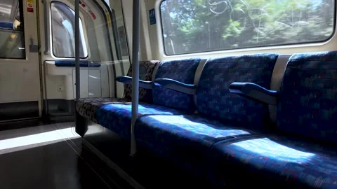 A quiet, empty row of blue patterned seats inside a modern London Underground Stock Footage 337874298