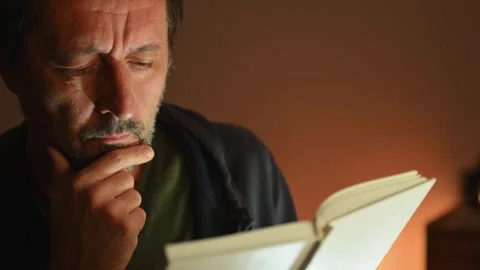Quiet moment of reflection - mature man absorbed in reading under warm low .. Stock Footage 332279807
