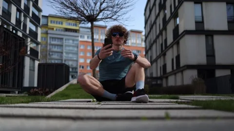 A quiet pause between city walls. A man sits on the pavement, arm extended with  Stock Footage 305999980