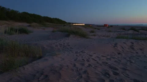 Quiet sandy beach at dusk with dune grass, footprints, calm sea, and soft Stock Footage 338134896