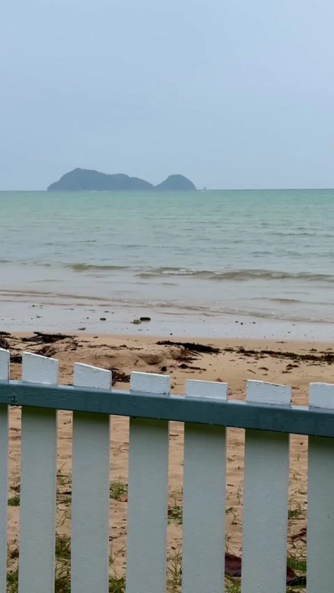 Quiet sandy beach with gentle waves and a distant island, viewed over a white Stock Footage 346428197