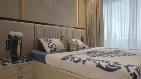 Quilted bed with patterned pillows and textured wall and flower vase on marble Stock Footage 328485692