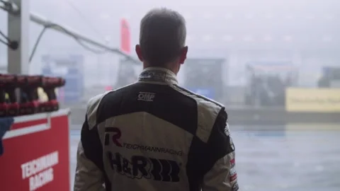 Race car driver in fireproof suit looking at foggy wet pitlane bad weather Video stock 132731660
