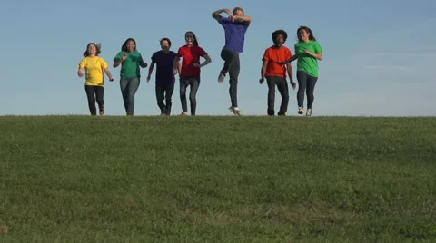 Racially-diverse students run over a hill and jump - wide Stock Footage 44117410