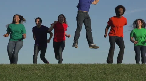 Racially-diverse students run over a hill and jump - mid Stock Footage 44117412