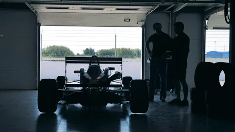 Racing car parked inside of a garage with two mechanics Stock Footage 162877783