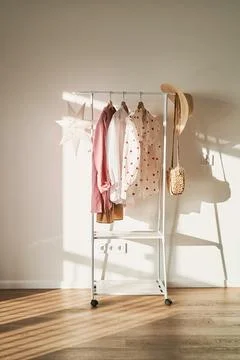 A rack of clothes in the rays of the bright sun against a white wall. Stock Photos