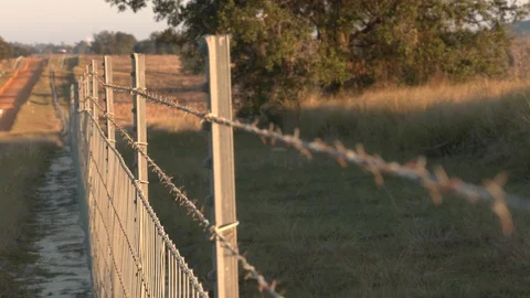 Rack focus of a barbed wire fenced dividing a pasture from a dirt road Stock Footage 124145038