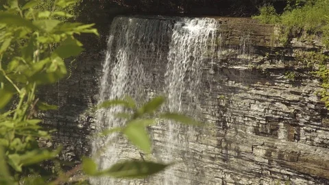 Rack focus from leaves on a tree to a beautiful waterfall. Stock Footage 78953479