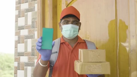 Rack focus shot, delivery boy with medical face mask and parcel in hand showing Stockbeeldmateriaal 169139714