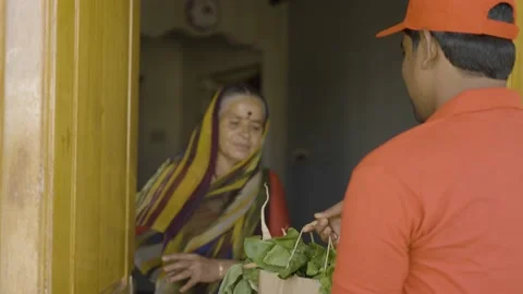 Rack focus shot, Indian delivery boy giving groceries to senior women after Stock Footage 169300309