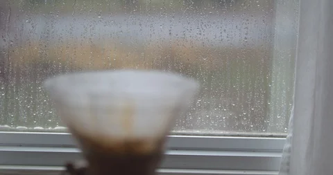 Rack Focus from a Steaming Chemex Coffee Filter to a Rain Droplet Covered Window Stock Footage 100096401