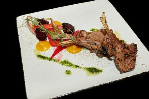 Rack of lamb. Fried or baked meat with vegetables in a plate on a black backg Stock Photos