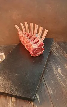 A rack of raw lamb chops arranged neatly on black slate, showing fine marbling Stock Photos