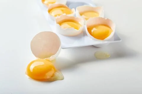 Rack for six broken eggs with whole yolks. One egg lies nearby, the yolk i... Stock-Fotos
