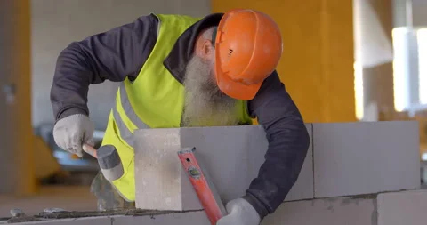 A racy builder with a beard  adjusts the aerated concrete block with a hammer Stock Footage 119625427