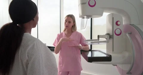 Rad tech in pink scrubs showing breast placement at mammogram to Stock Footage 335570390