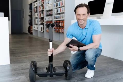Radiant store manager holding hoverboard and smiling into camera Stock Photos