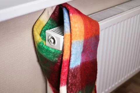 A radiator wrapped in a multi-colored scarf, symbolizing the cold in the room Stock Photos