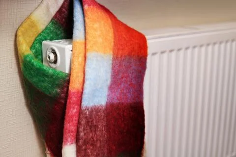 A radiator wrapped in a multi-colored scarf, symbolizing the cold in the room Stock Photos