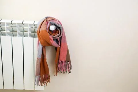 The radiator is wrapped in a multicolored warm scarf. Space for text. Stock Photos