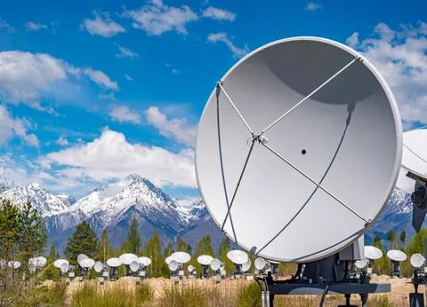 Radio telescope array stands in a field with snow-capped mountains under a clear Stock Photos