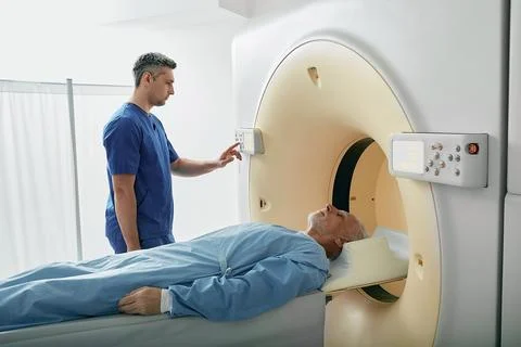 Radiographer operating computed tomography scanner being used to scan lying p Stock-Fotos
