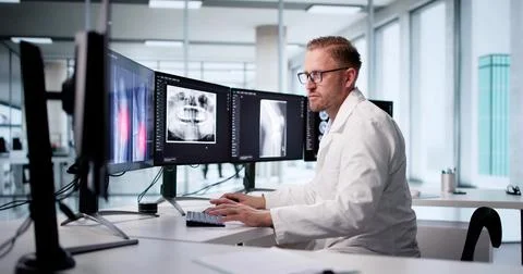 Radiologist Analyzing Patient X-ray On Computer Screen In Hospital Setting. Stock Photos