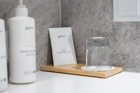 A Radisson branded shower cap and glass sit on a wooden tray in a modern hotel Stock Photos