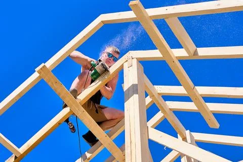 Rafter assembly, young builder trims wooden member using electric circular .. Stock Photos