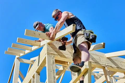 Rafter legs aligned by two workers as one worker drives screws with cordles.. 库存照片