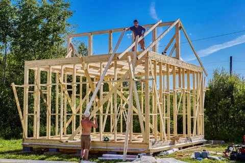 Rafter system installation, young worker positions timber rafters on frame .. Stock Photos