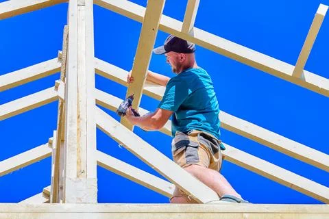 Rafters form timber roof framework as young construction worker drives a sc.. Stock Photos