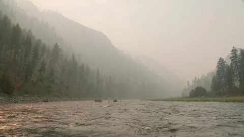 Rafts floating down a river through forrest filled with smoke from fire Stock Footage 80635486