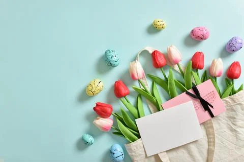 A rag eco-bag with Easter eggs and bouquets of tulips on a light blue backgro Stock Photos