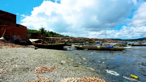 Ragged boats and trash float in the water near a slum in Salvador Stock Footage